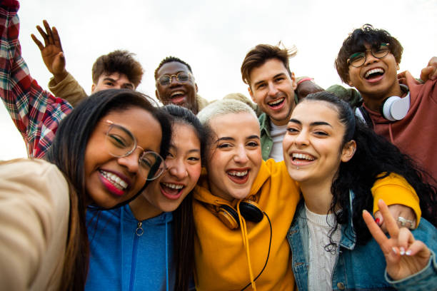 finicial Group of multiracial teen college friends having fun outdoors. Happy people taking selfie. Gen z, friendship and technology concept.