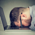 Side view of chubby man looking broken while lying on top of laptop.