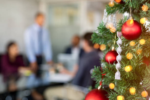 Close up of decorated christmas tree in office with business people working in background. Xmas celebration in corporate office. Detail of christmas balls and lights with working office.