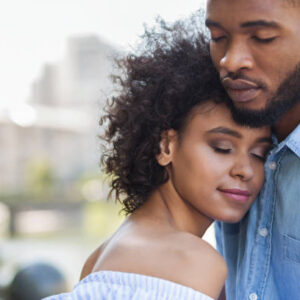 Tender black couple hugging with closed eyes outdoors