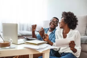 personal finance Family insurance concept. Positive black couple reading documentation at home, checking agreement details together. Young African Couple Sitting On Sofa Calculating Invoice