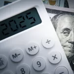 Text 2025 on calculator screen with one hundred dollar bill Benjamin Franklin looking at. Tax business concept