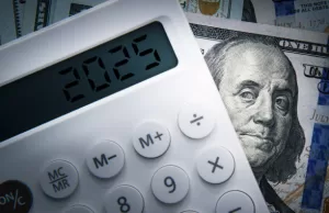 5 Reasons to Be Optimistic About the 2025 Economy. Text 2025 on calculator screen with one hundred dollar bill Benjamin Franklin looking at. Tax business concept