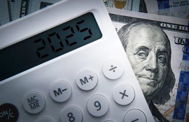 Text 2025 on calculator screen with one hundred dollar bill Benjamin Franklin looking at. Tax business concept